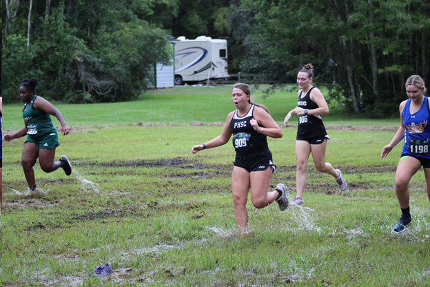 Runners race through wet and muddy grass track.
